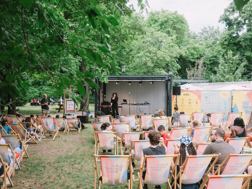 KVSAL performt bei der Kultursommer-Bühne im Waldmüllerpark. Menschen sitzen in Liegestühlen vor der Bühne. 