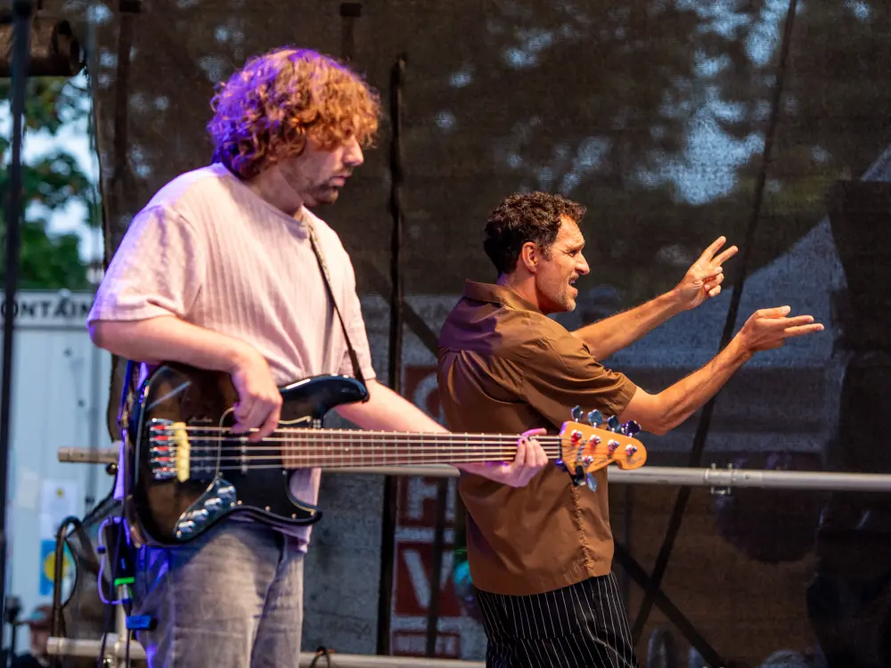 Ein Gebärdenperformer und der Bassist von Cordoba78 stehen auf einer Bühne. 