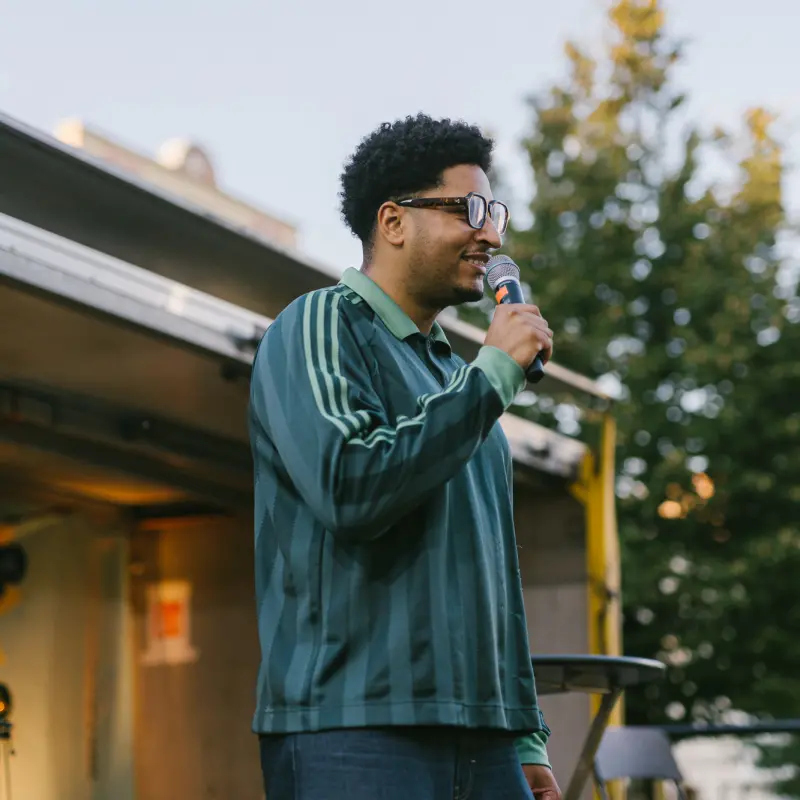 Marvin Tare: Marvin Tare spricht in ein Mikrofon. Er zeigt sein Ausschnitte seines Kabarett-Programms auf der Kultursommer-Bühne beim Ottakringer Bierfest.