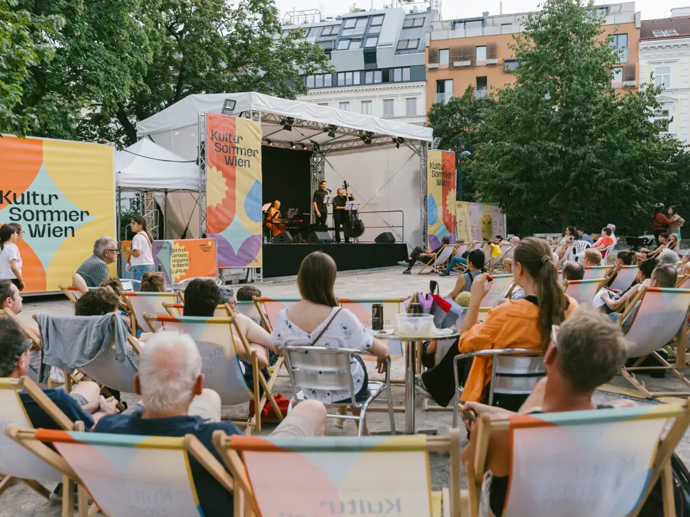 Libercuatro tango ensemble: Menschen sitzen im Reithofferpark und hören dem Libercuatro tango ensemble auf der Kultusommer-Bühen zu.