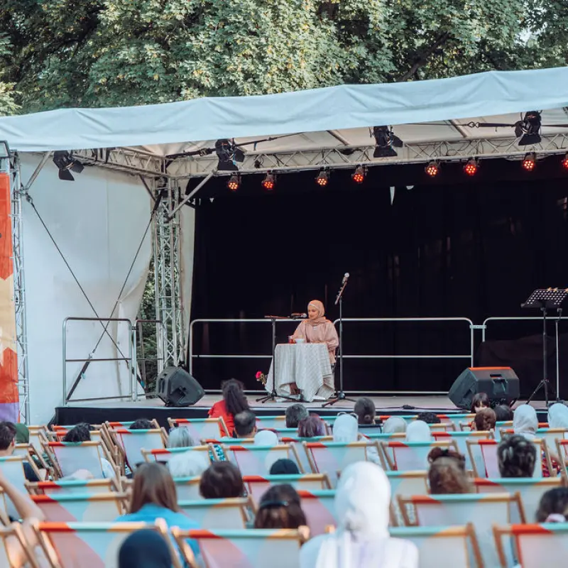 Nora Hamed: Nora Hamed sitzt an einem runden Tisch und liest auf der Kultursommer-Bühne.