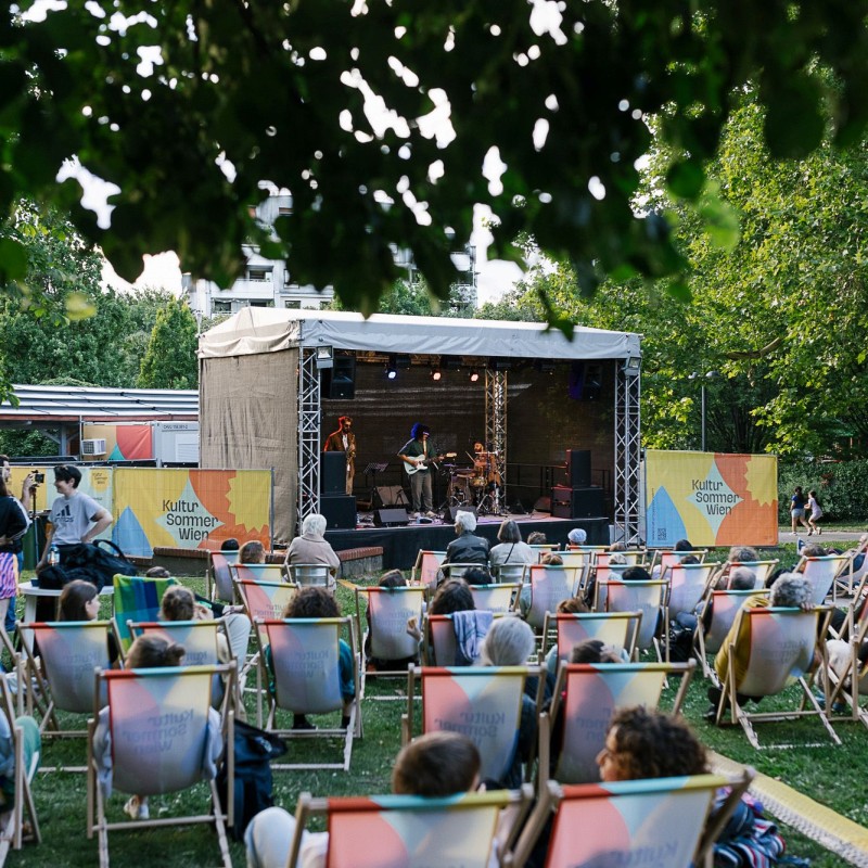 Foto: Theresa Wey Blick auf die Bühne im Wilhelmsdorfer Park. Vor der Bühne sitz das Publikum in Liegestühlen.