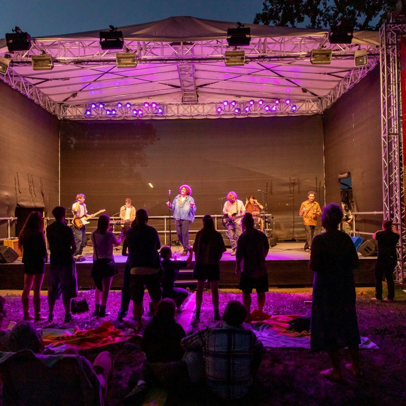 Foto: Judith Stehlik Cordoba78 und Gebärdenperformer Günter Roiss treten auf der Kultursommer-Bühen im Stadtpark Atzgersdorf auf. Der Abend bricht herein. Die Bühne ist mit Scheinwerfern ausgeleuchtet. 