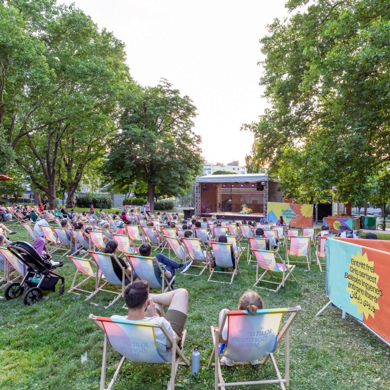 Foto: Judith Stehlik Blick auf die Bühne im Wilhelmsdorfer Park. Das Publikum sitzt davor in Liegestühlen. Aboli Dhayarkar tanzt auf der Bühne in traditionellem Indischen Gewand.