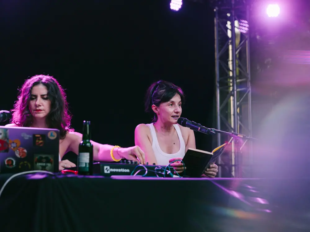Ana Drezga & Scharmien Zandi: Ana Drezga & Scharmien Zandi bei einer Lesung auf der Kutursommer-Bühne. Ana Drezga liest aus dem Buch "Top Girls". Scharmien Zandi sitzt vor einem Computer und macht elektronische Beats. 
