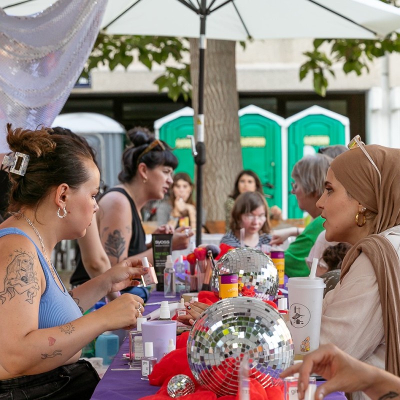 Zwei Frauen sitzen an einem Tisch einander gegenüber. Die eine macht der anderen die Nägel. Es handelt sich um die Styling Corner am Schrödinger Platz im Rahmen von Kultursommer Plus.