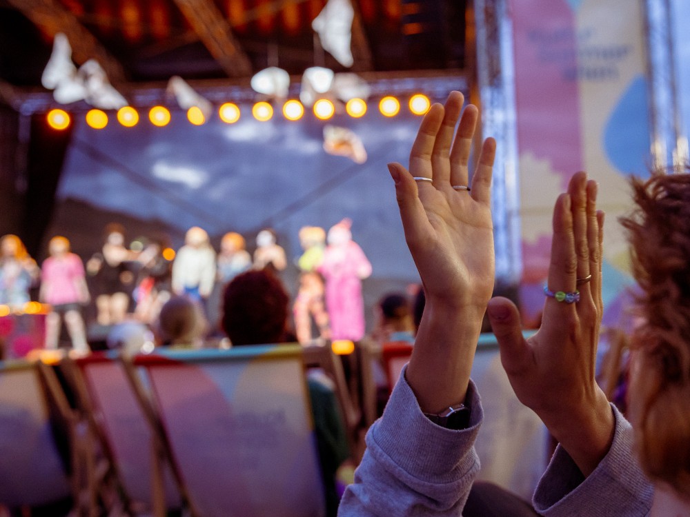 Eine Person klatscht in die Hände, dahinter die Silhouetten der Performer:innen von House of Clits.