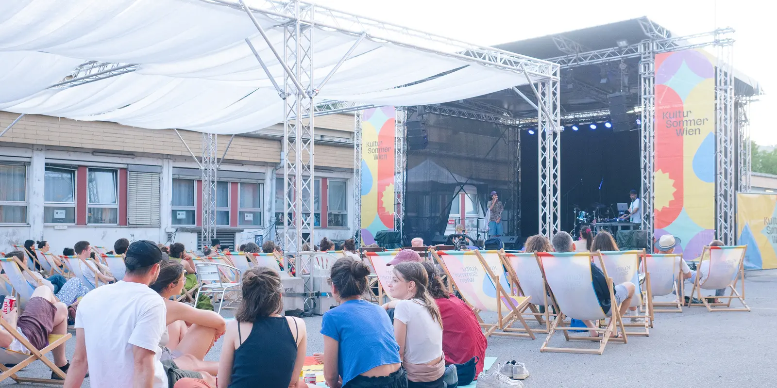 : Menschen sitzen in Liegestühlen und auf Picknickdecken vor de
Kultursommer-Bühne beim Nordwestbahnhof.