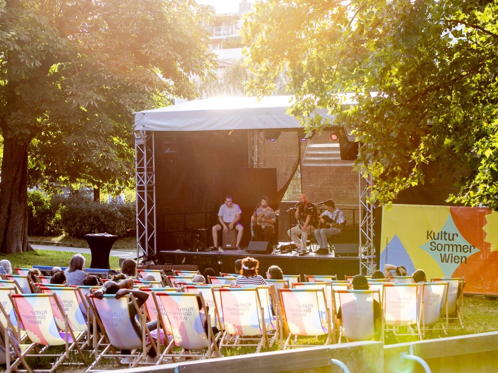 Blick auf die Bühne im Wilhelmsdorfer Park. Das Publikum sitzt in Liegestühlen. Auf der Bühne spielt die Band Teschek ein Konzert.