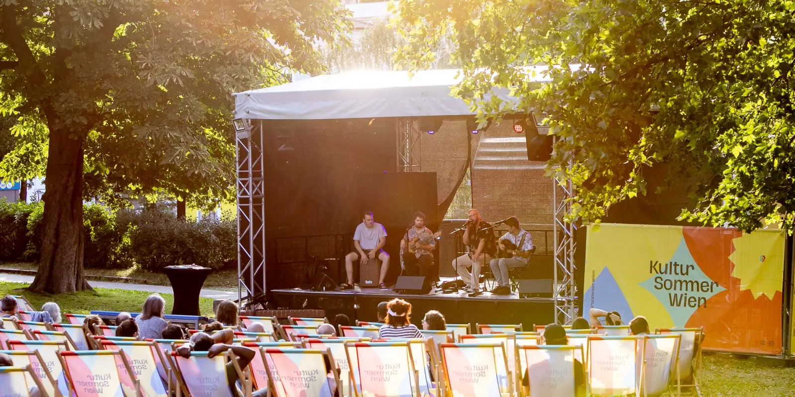 Teschek: Blick auf die Bühne im Wilhelmsdorfer Park. Das Publikum sitzt in Liegestühlen. Auf der Bühne spielt die Band Teschek ein Konzert.