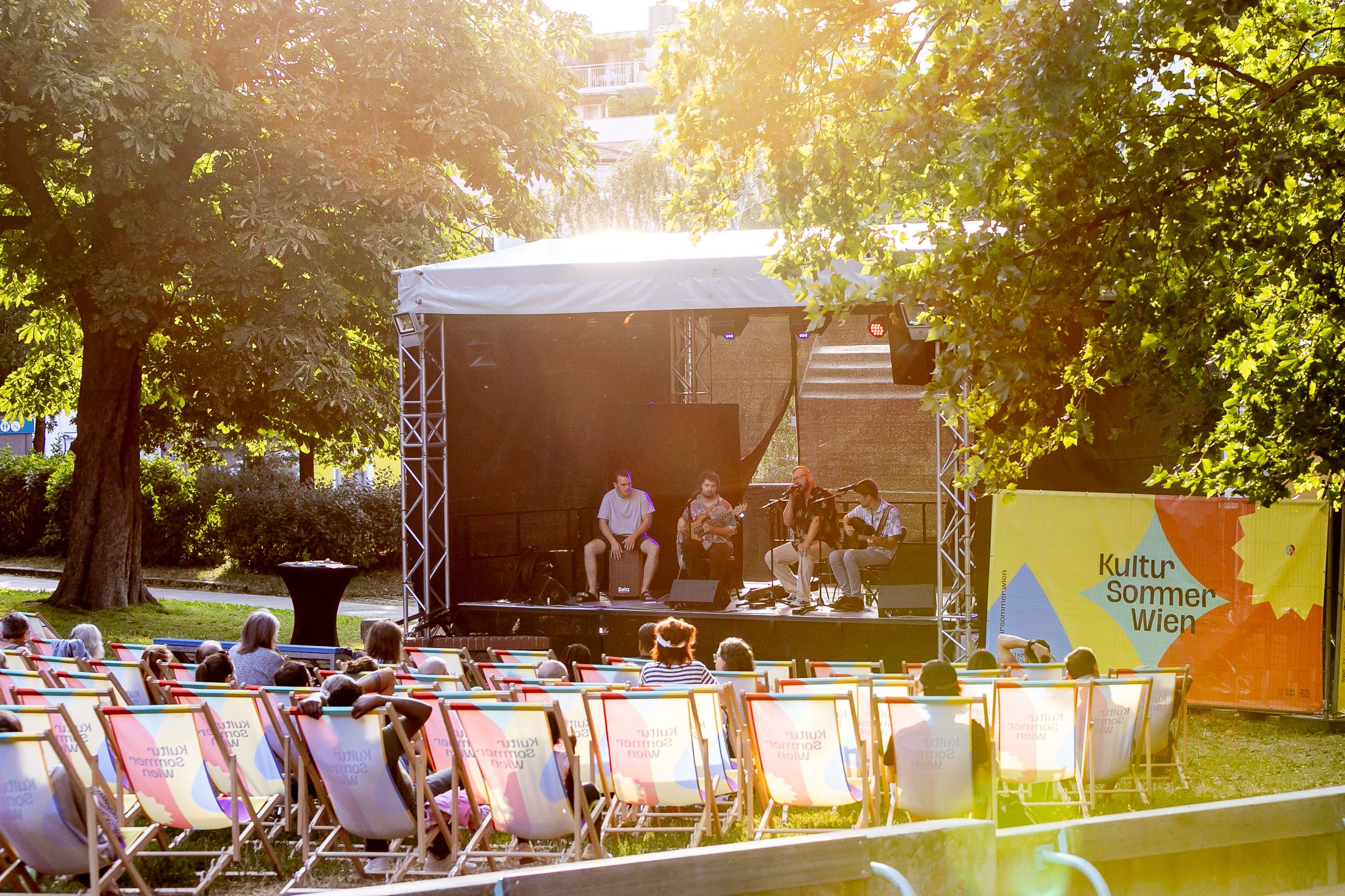 Blick auf die Bühne im Wilhelmsdorfer Park. Das Publikum sitzt in Liegestühlen. Auf der Bühne spielt die Band Teschek ein Konzert.
